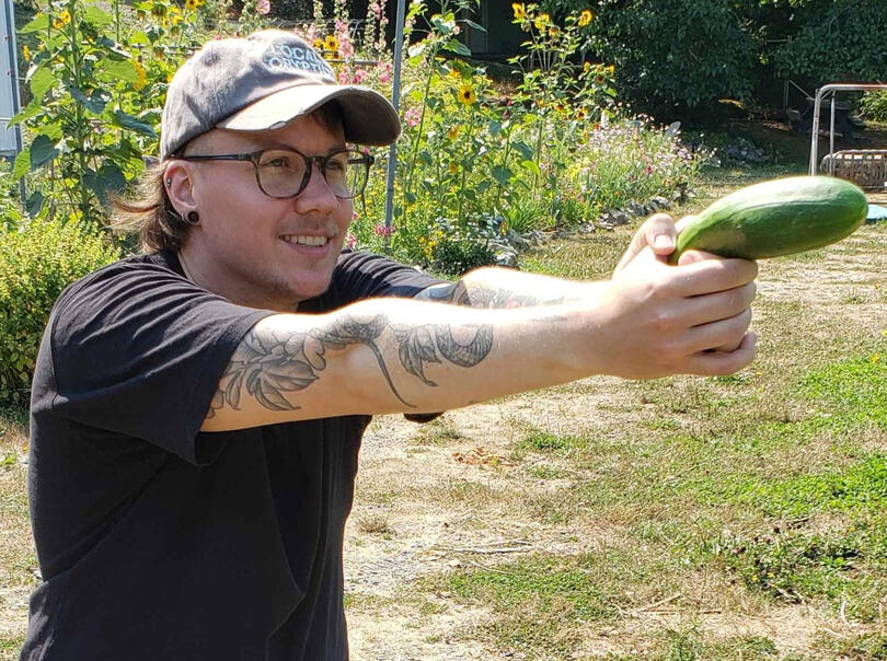 Jesse Campbell smiling holding a cucumber like a laser gun